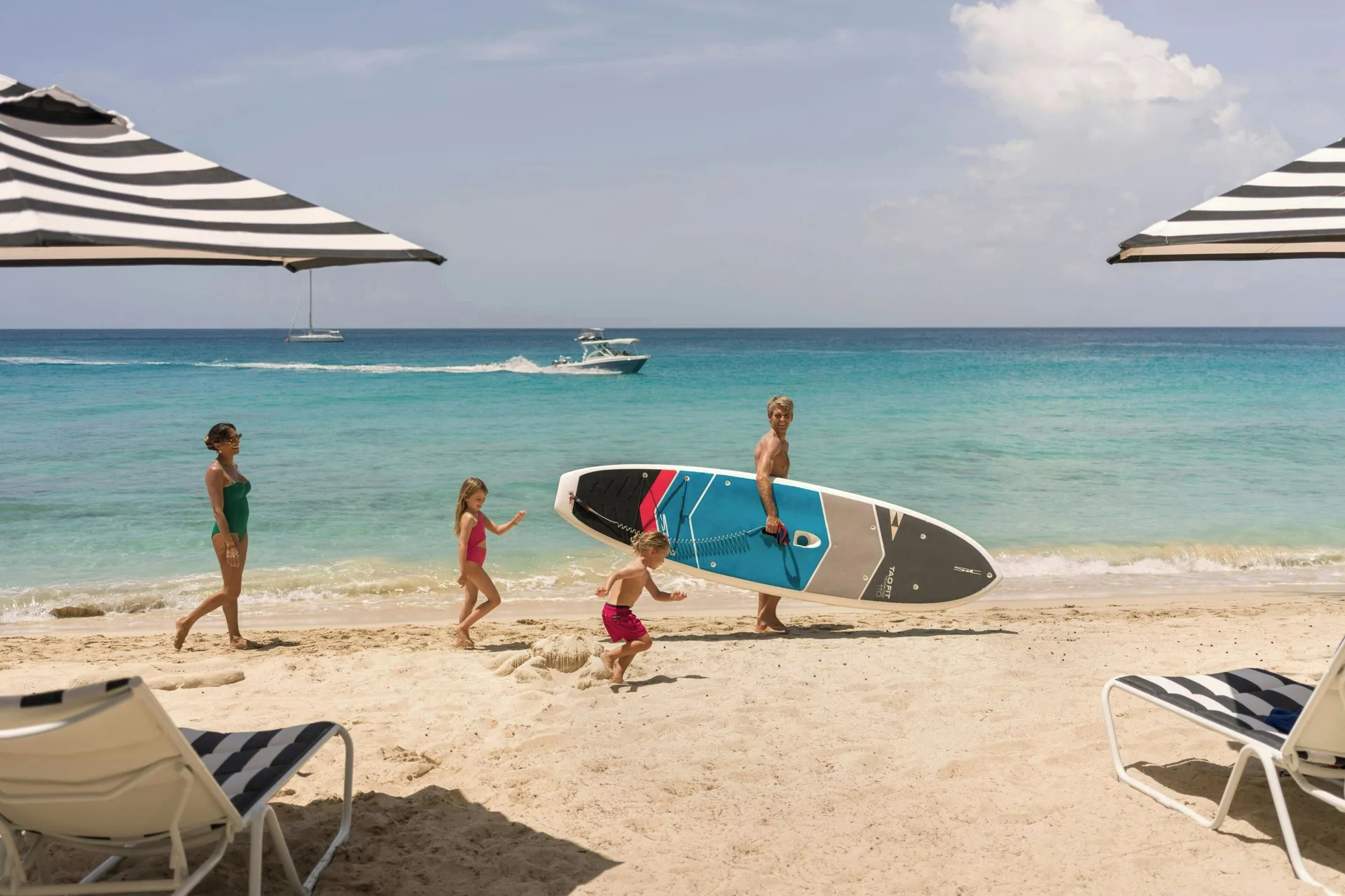 Family walking on the beach with a paddleboard at Colony Club, Barbados.