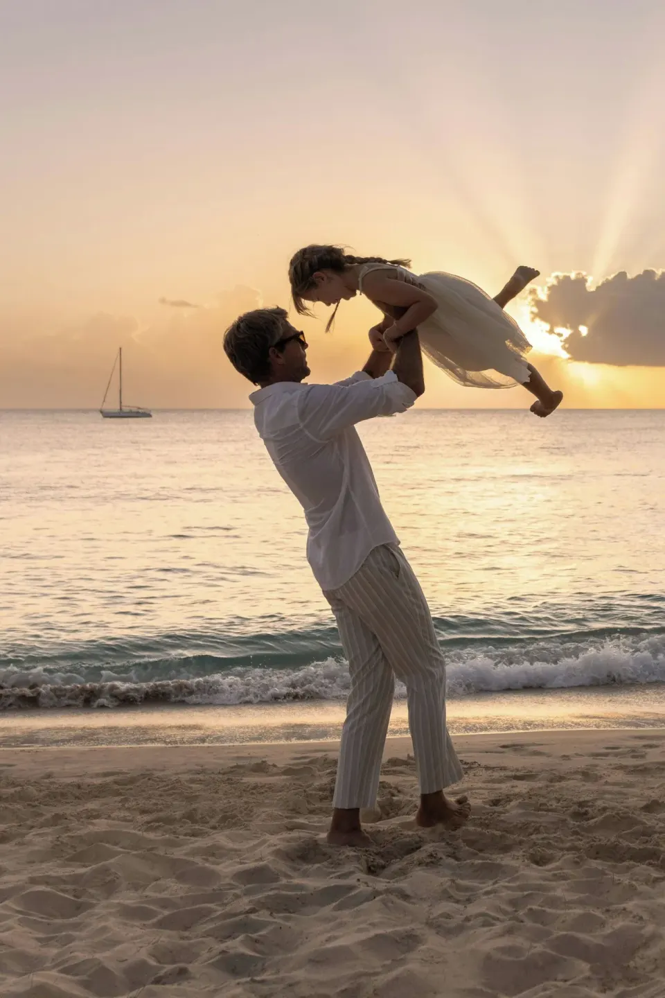 Man lifting a child on the beach at sunset at Colony Club, Barbados.