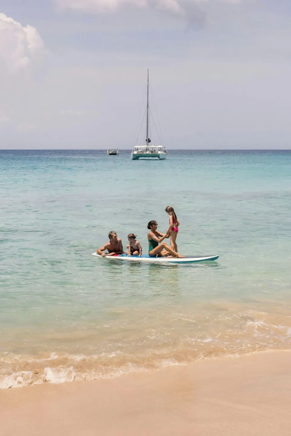 A family paddles in clear shallow sea with boats offshore at Colony Club, Barbados.