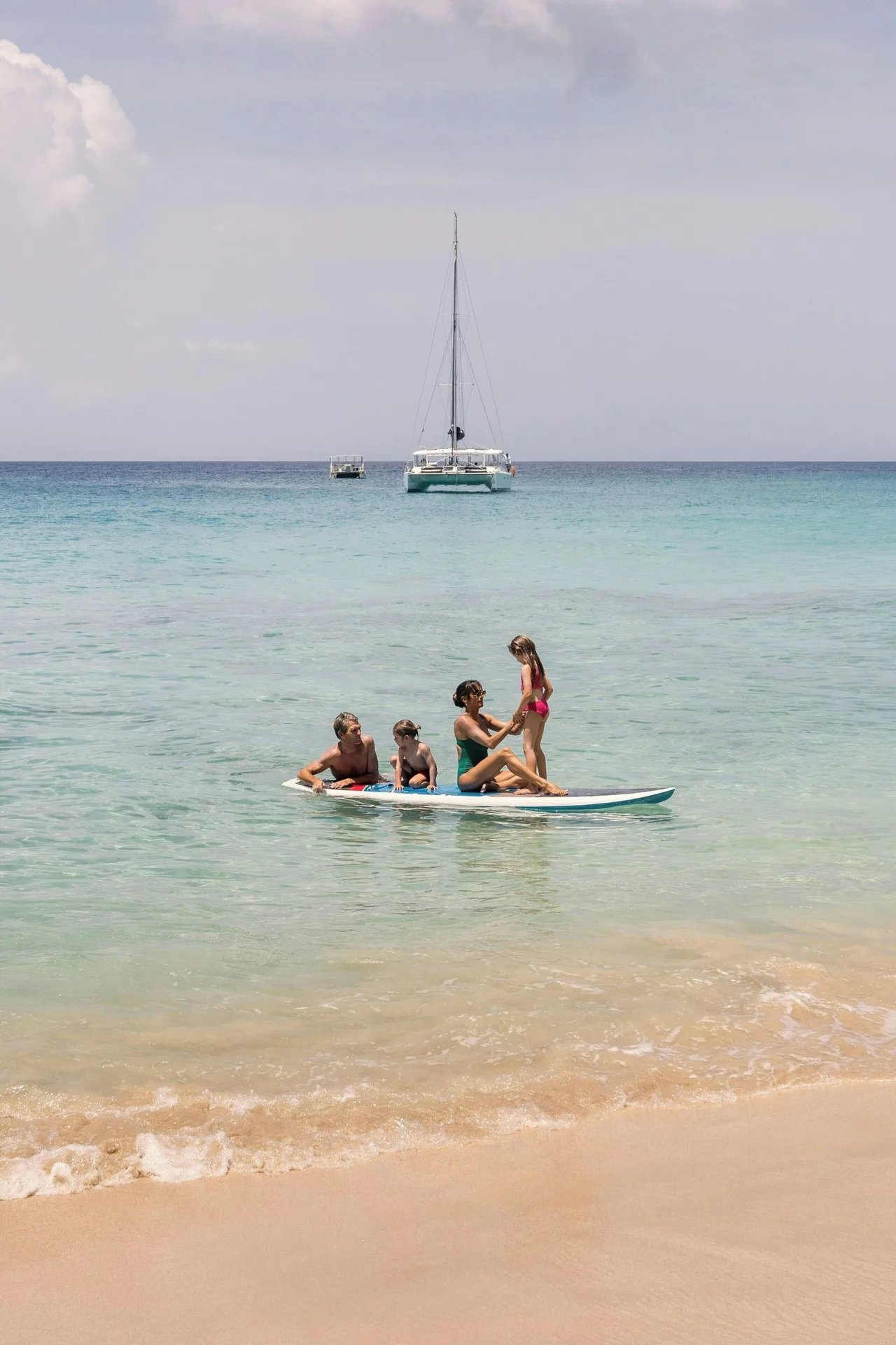 A family paddles in clear shallow sea with boats offshore at Colony Club, Barbados.