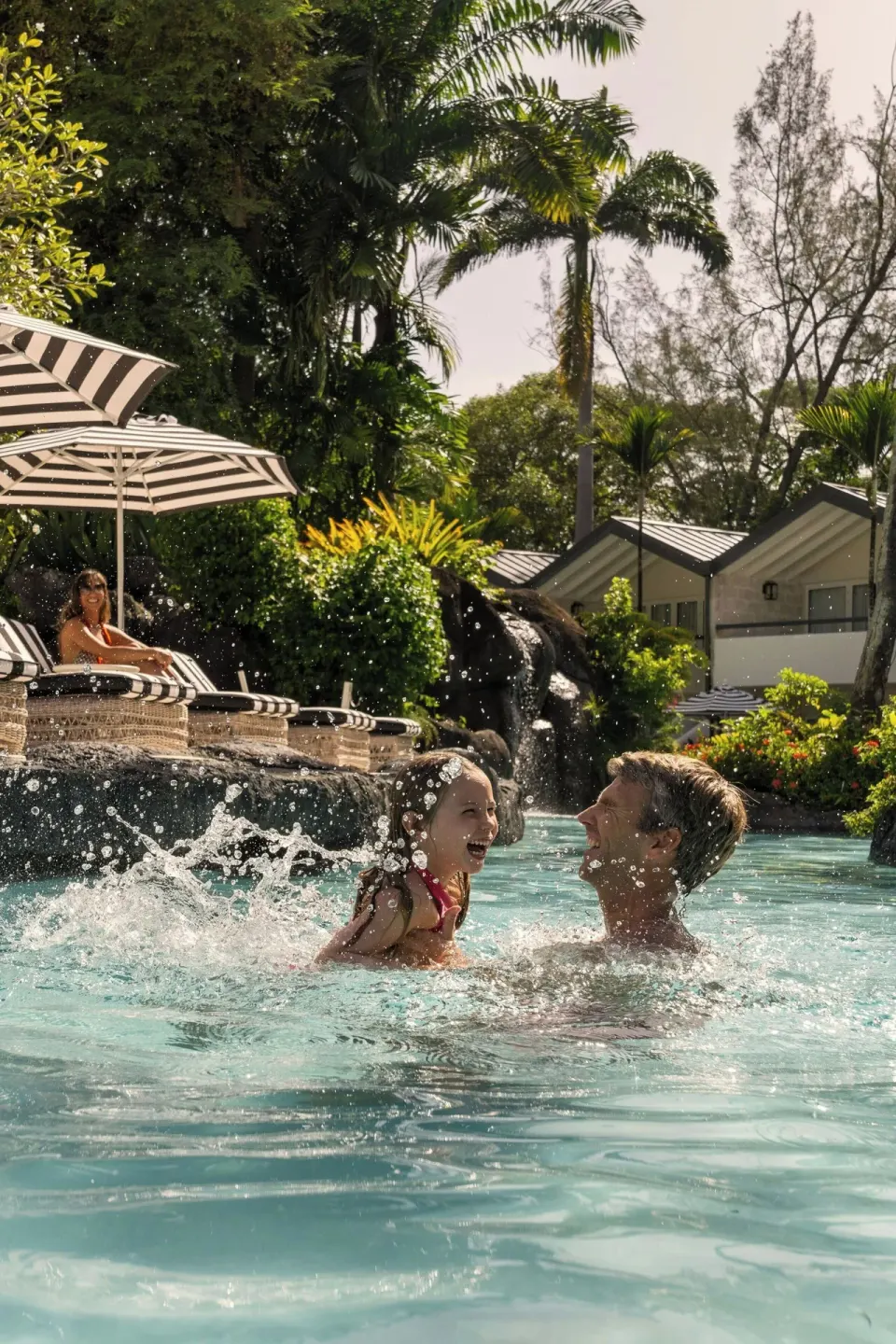 Guests splashing in a lagoon-style pool with palms and loungers at Colony Club, Barbados.