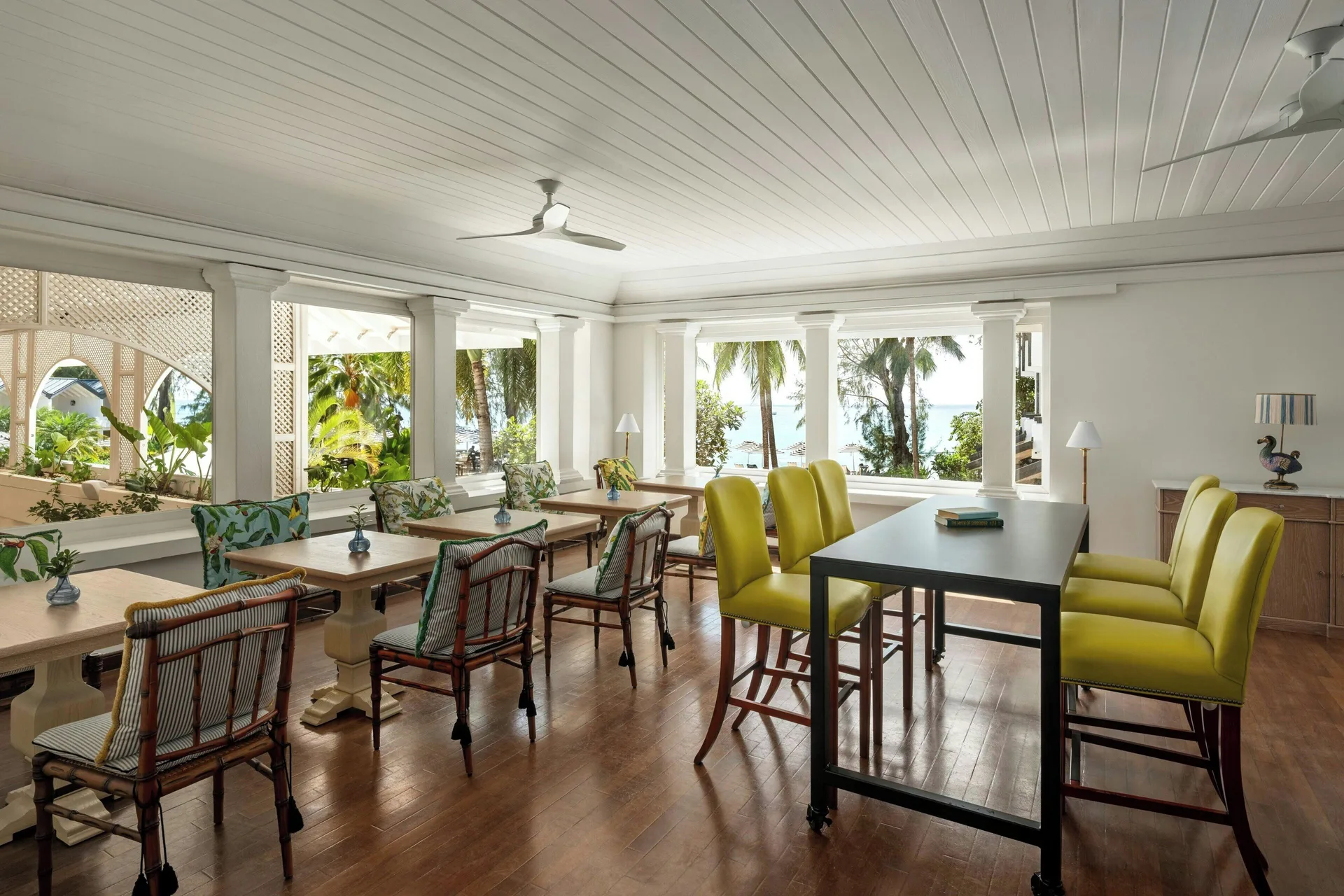 Open lounge with tables, bright chairs and sea glimpses at Colony Club, Barbados.