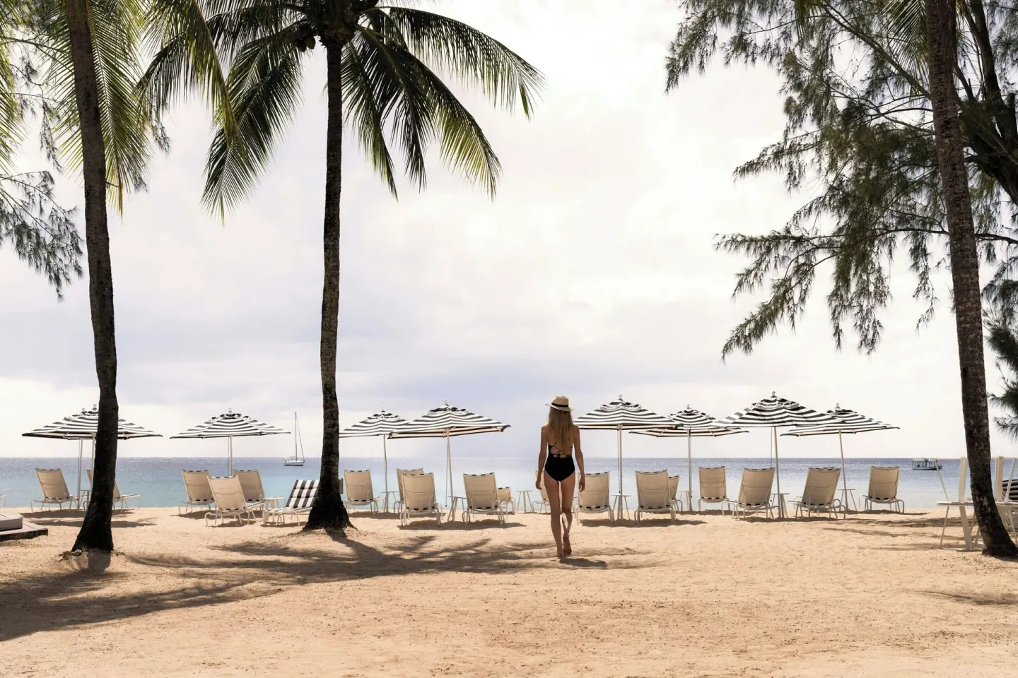 A guest walks across the sandy beach toward striped umbrellas at Colony Club, Barbados.