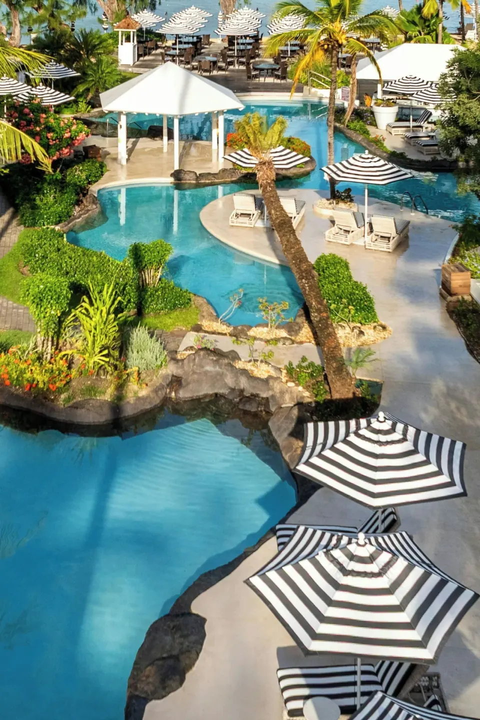 Elevated view of winding lagoon pools and striped umbrellas at Colony Club, Barbados.