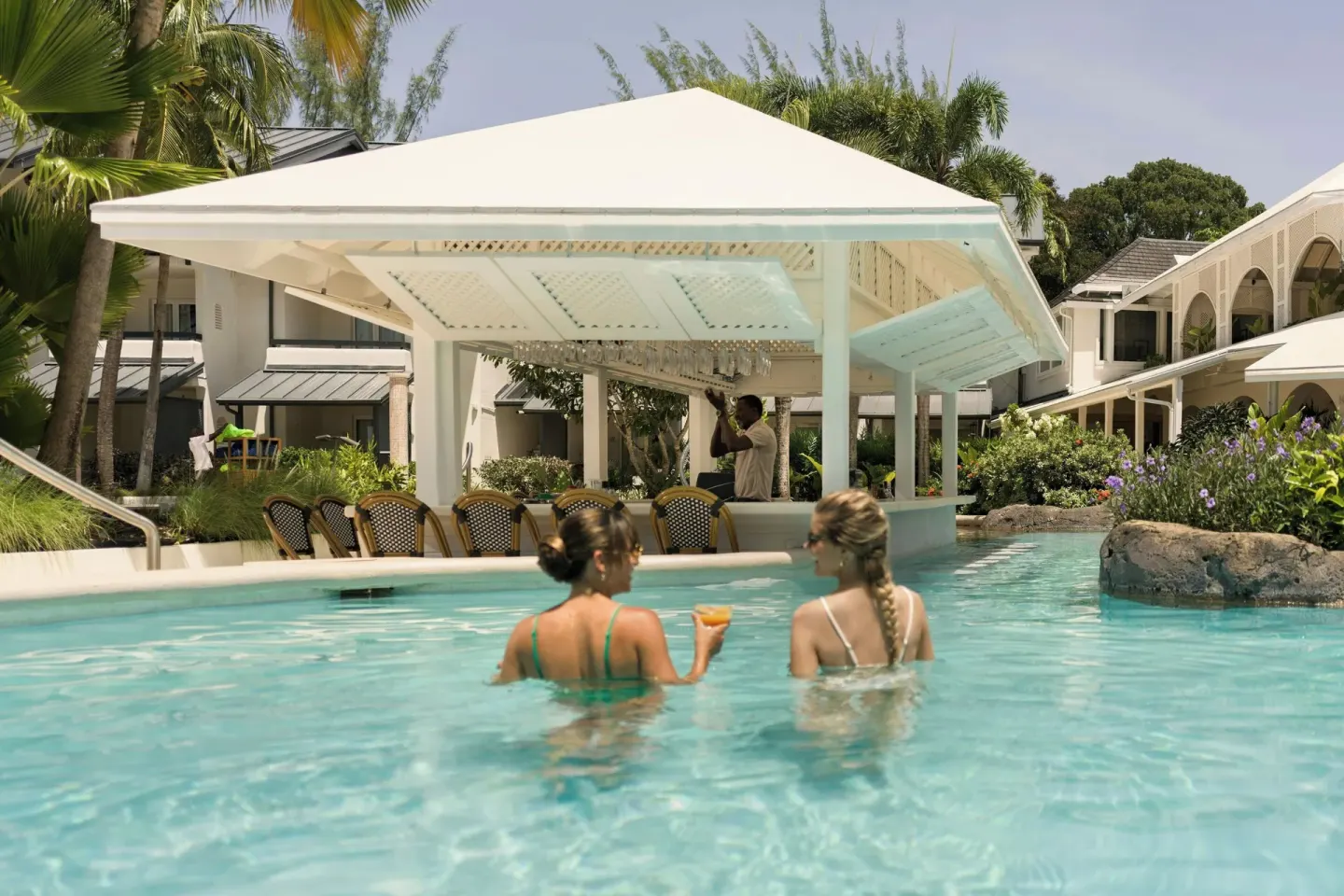 Guests stand in the pool by a swim-up bar with a white canopy at Colony Club, Barbados.