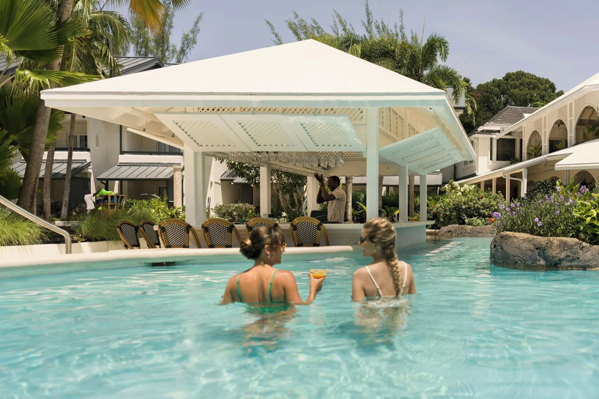 Guests stand in the pool by a swim-up bar with a white canopy at Colony Club, Barbados.