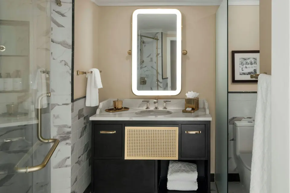 Suite bathroom vanity with lit mirror and glass shower at Colony Club, Barbados.
