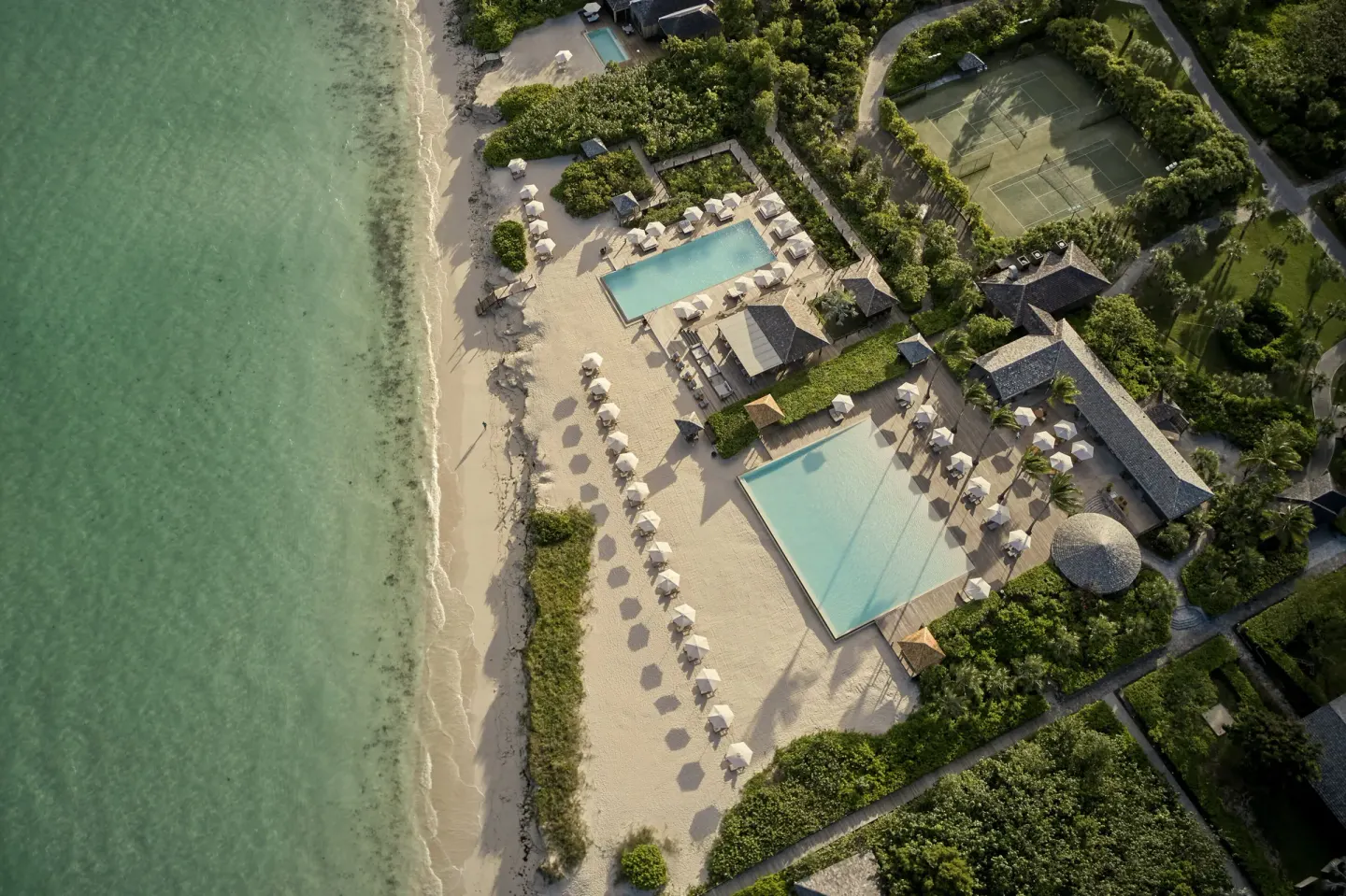 Aerial view of beachfront pools, umbrellas and tennis courts at COMO Parrot Cay.