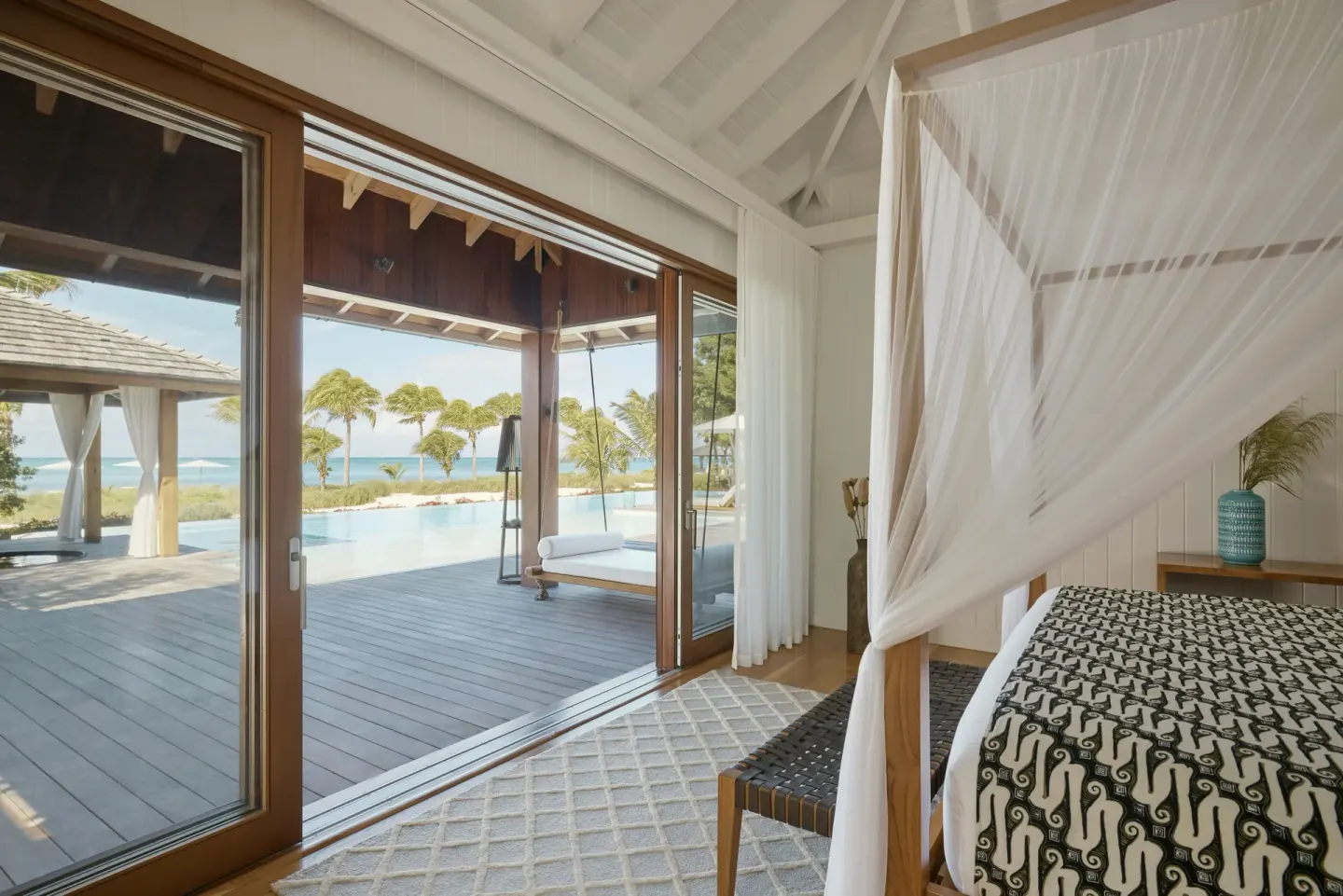 A bedroom with a draped bed opening to a pool and ocean view at COMO Parrot Cay.