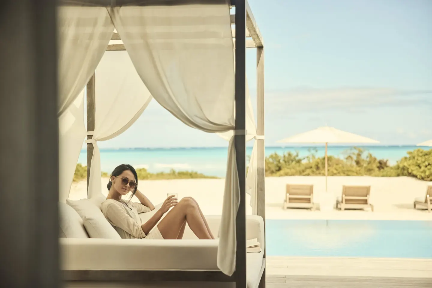 Poolside daybed at COMO Parrot Cay with a guest relaxing beside the beach and turquoise sea.