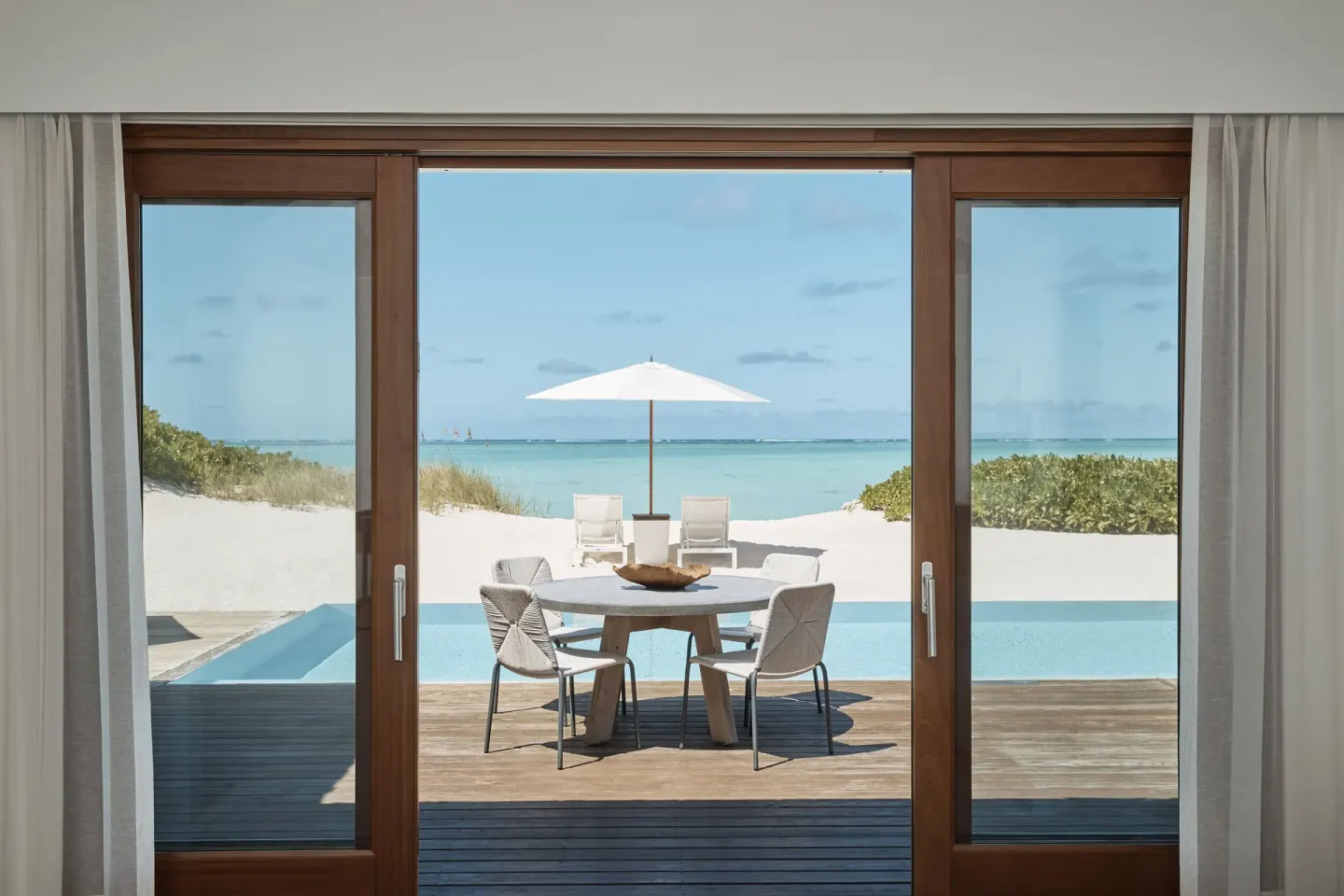 Beachfront deck with pool, dining table, umbrella and ocean at COMO Parrot Cay.