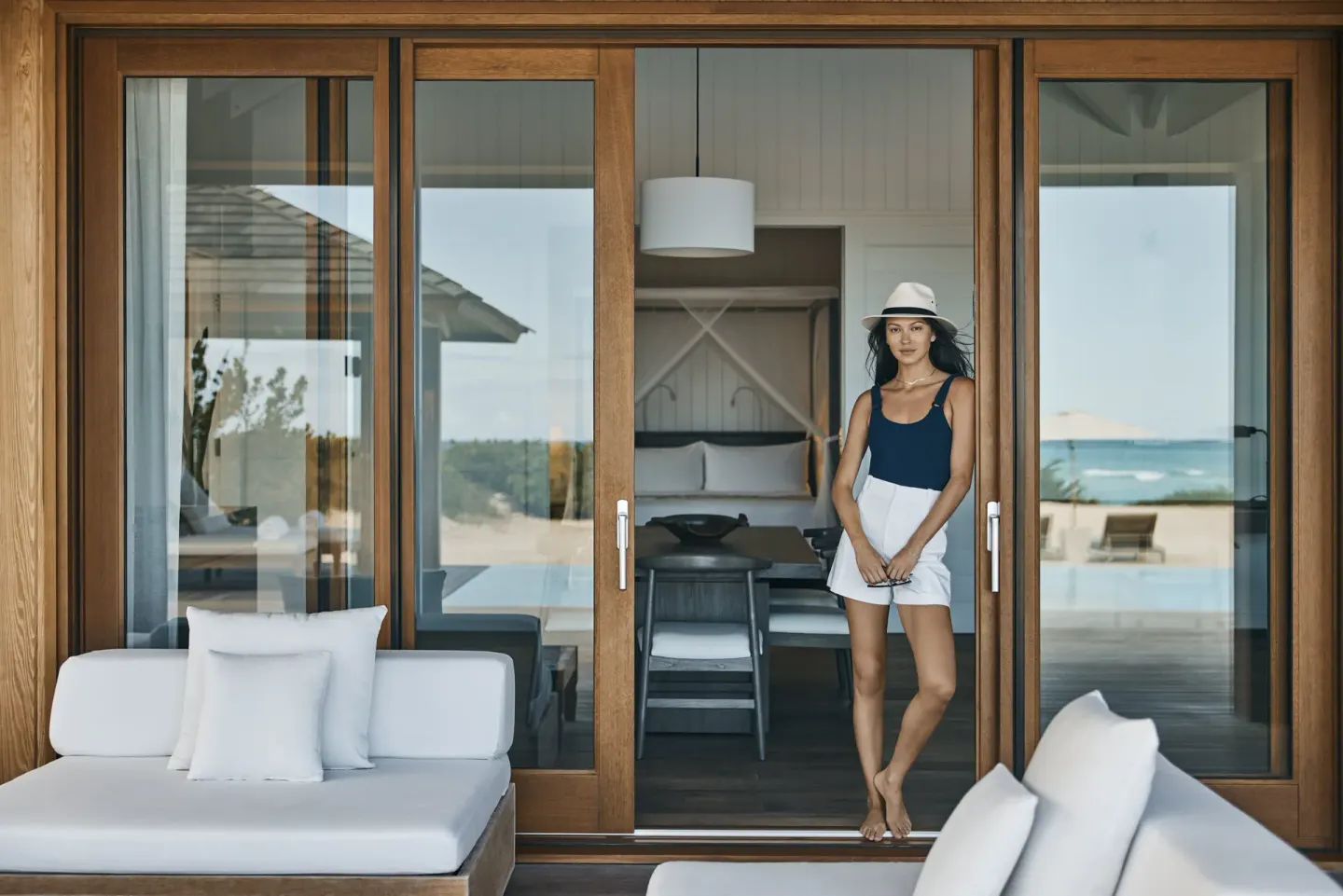 A guest stands by glass doors between a terrace and bedroom at COMO Parrot Cay.