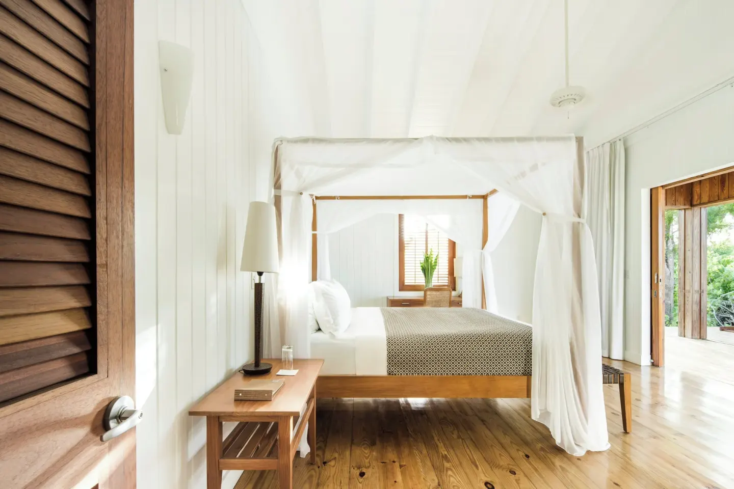 Canopy bed in a bright guest room at COMO Parrot Cay with wood floors and open terrace doors.