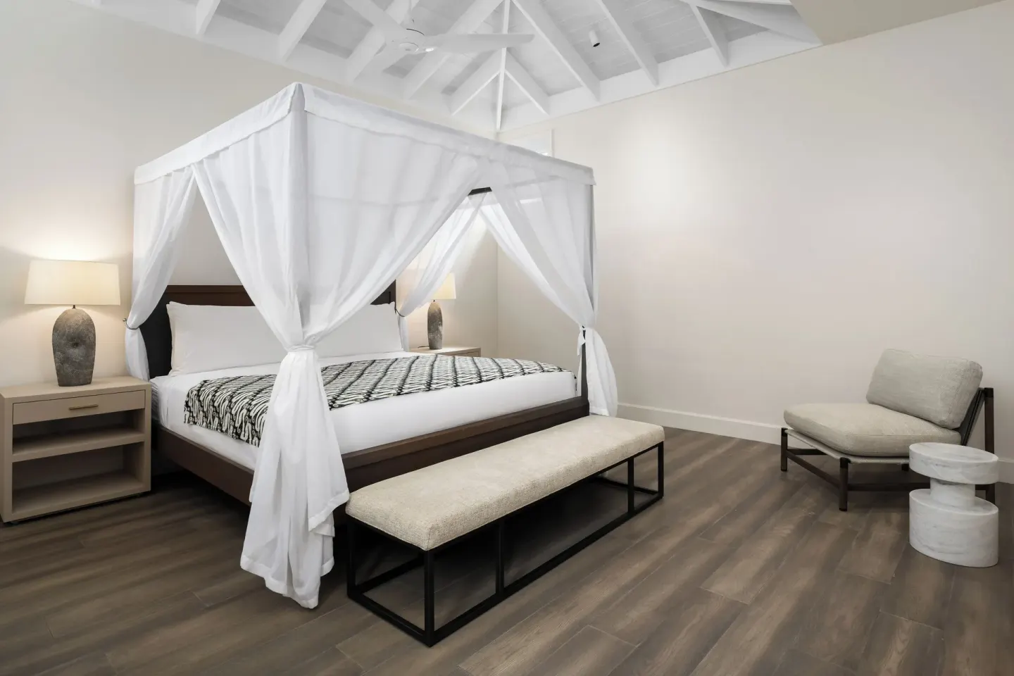 Guest bedroom at COMO Parrot Cay with a white canopy bed, bench, lounge chair, and vaulted ceiling.