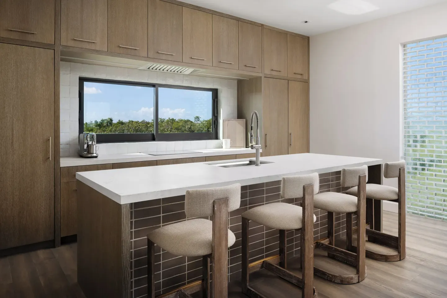 Modern kitchen at COMO Parrot Cay with an island, stools, wood cabinets, and a window view.