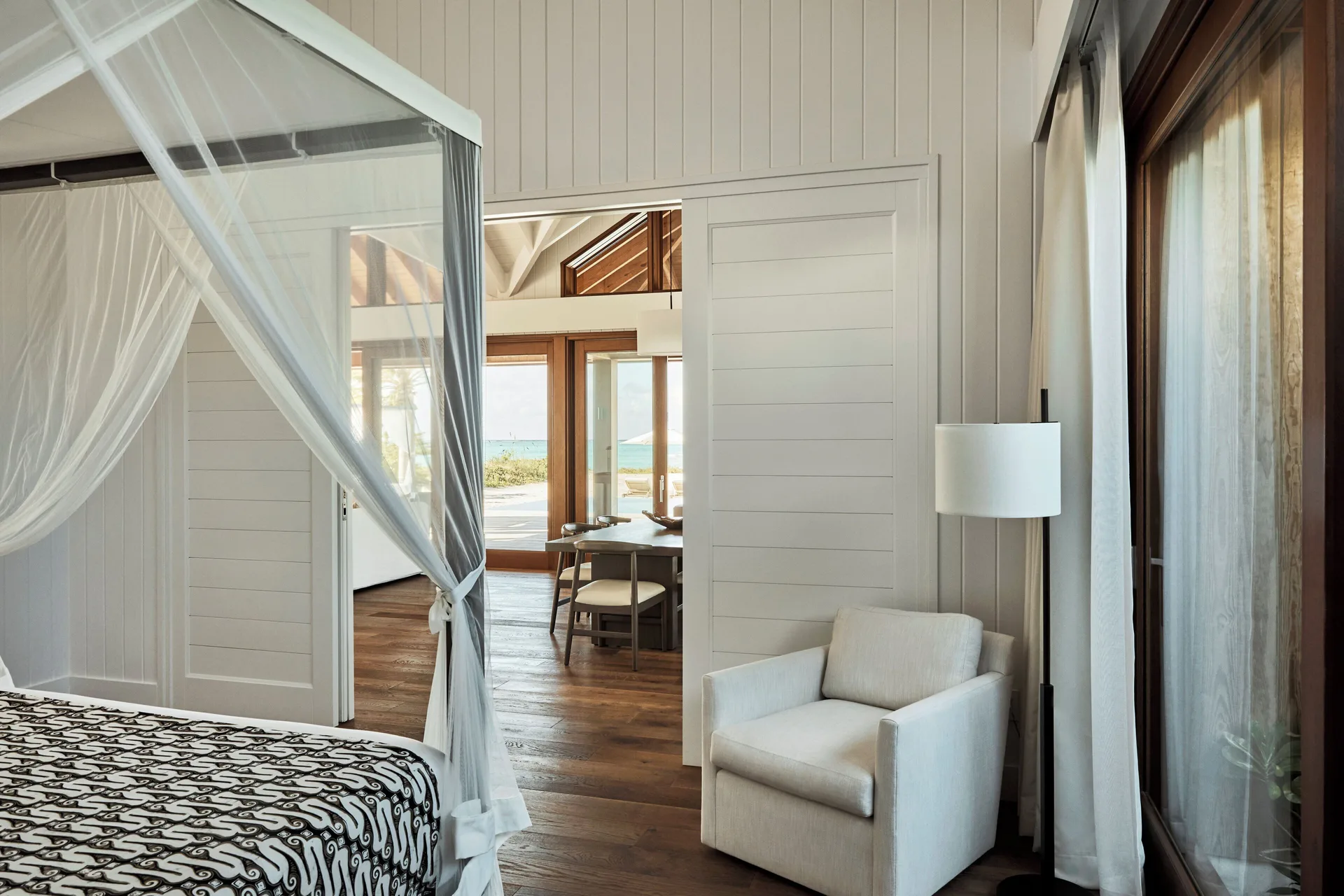 Canopy bed and sitting chair in a guest room at COMO Parrot Cay with ocean glimpses beyond.