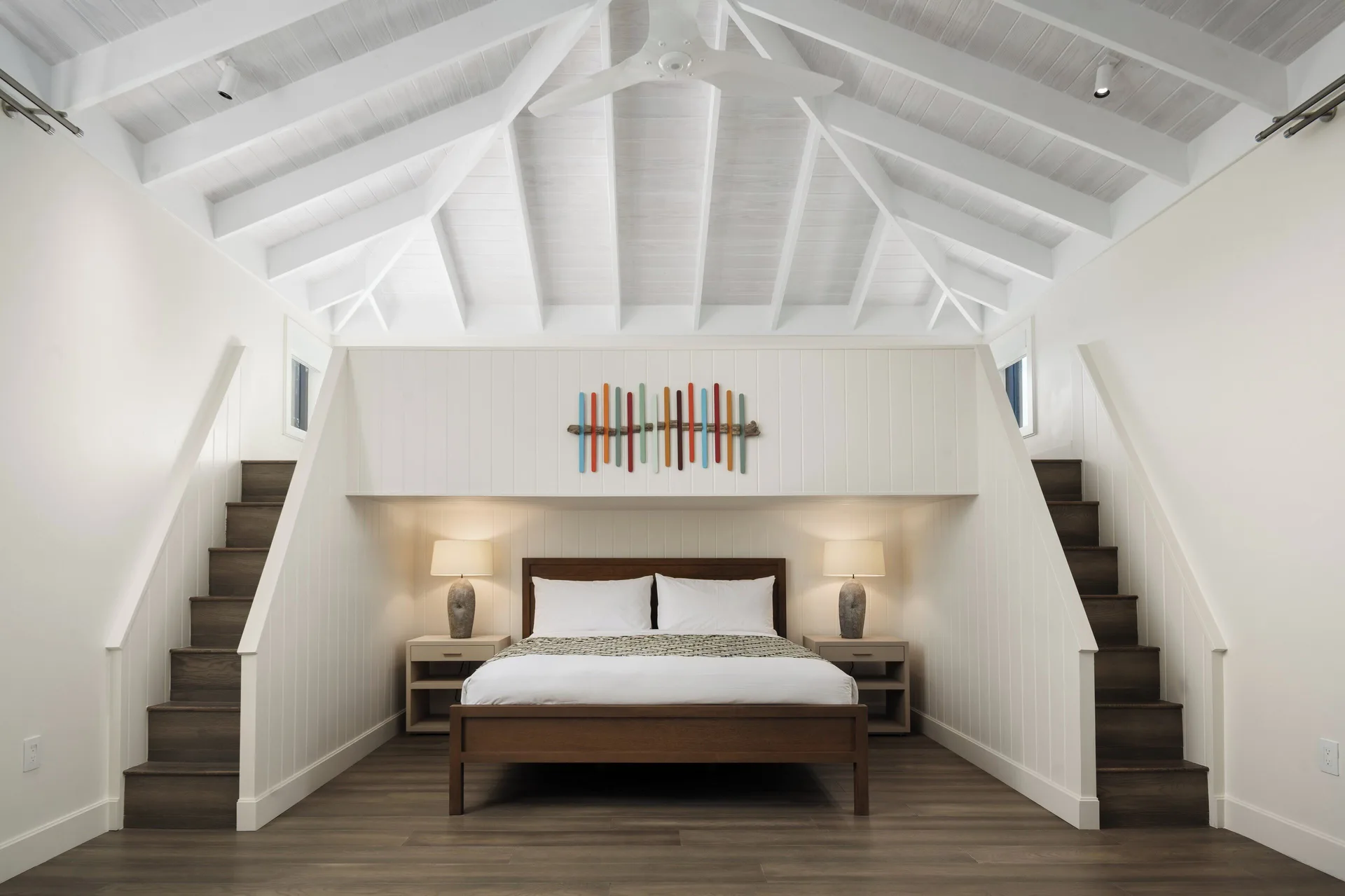 Loft-style bedroom at COMO Parrot Cay with a bed beneath twin staircases and a vaulted white ceiling.