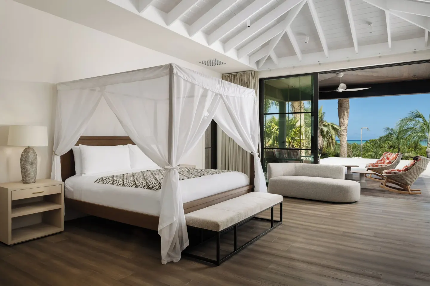 Spacious bedroom at COMO Parrot Cay with a canopy bed, lounge area, and terrace facing the sea.