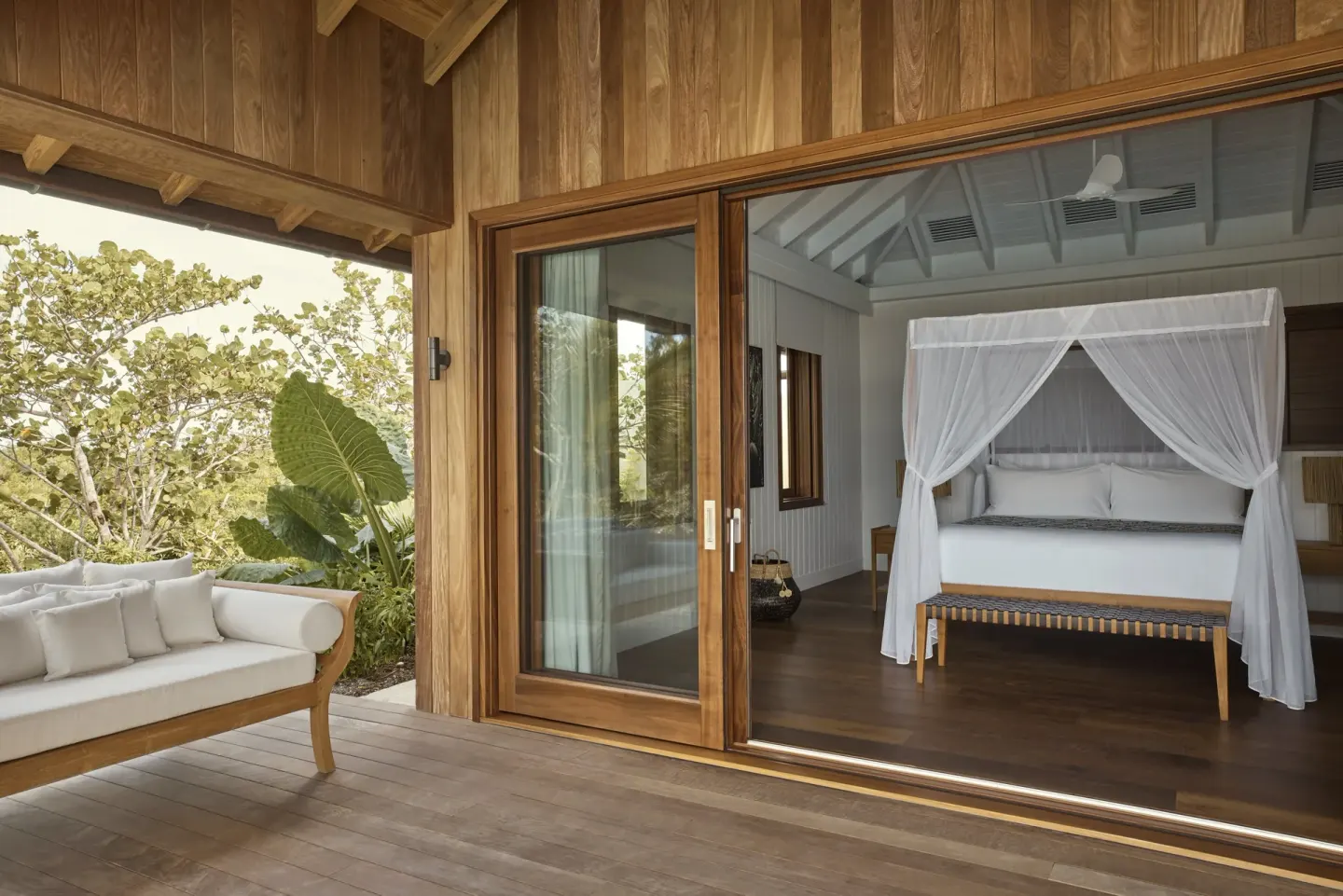 Covered terrace and bedroom at COMO Parrot Cay with a canopy bed visible through sliding glass doors.
