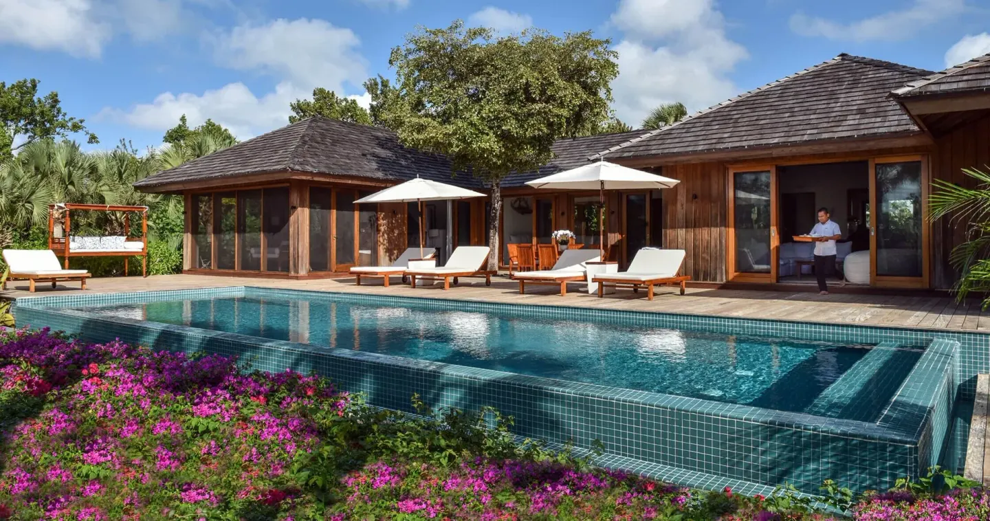 A timber villa with a long pool, loungers and flowering plants at COMO Parrot Cay.