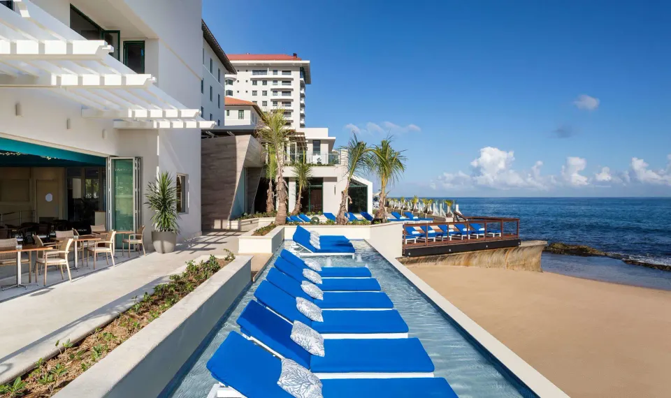 Blue lounge chairs beside a narrow pool and beach at Condado Vanderbilt Hotel.