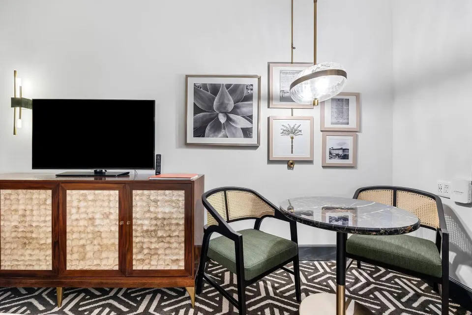 Guest room dining nook with round table, chairs, TV and artwork at Condado Vanderbilt Hotel.