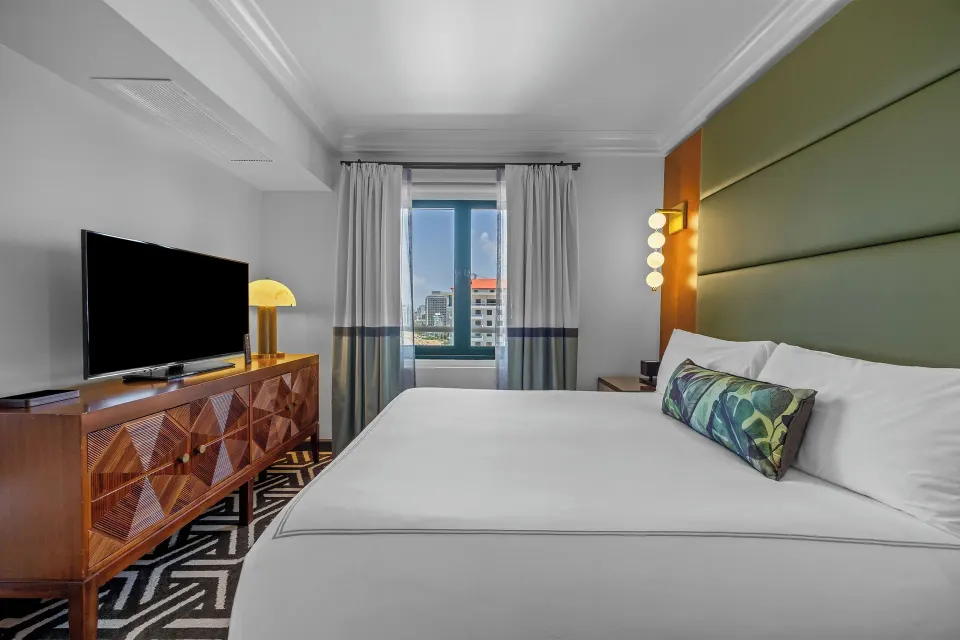King bed, TV console, and city-facing window in a guest room at Condado Vanderbilt Hotel.