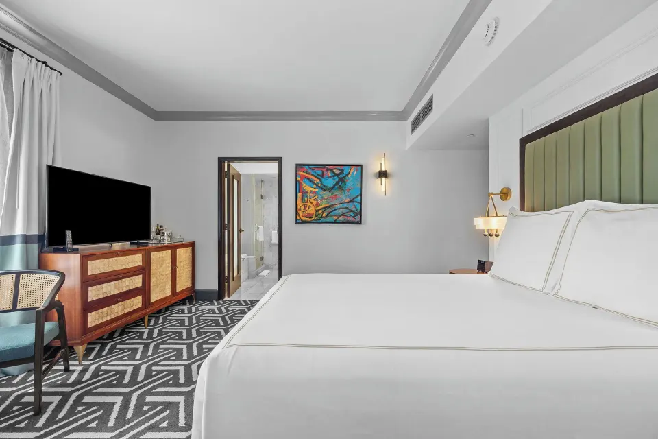 King bed, TV console, and colorful wall art in a guest room at Condado Vanderbilt Hotel.