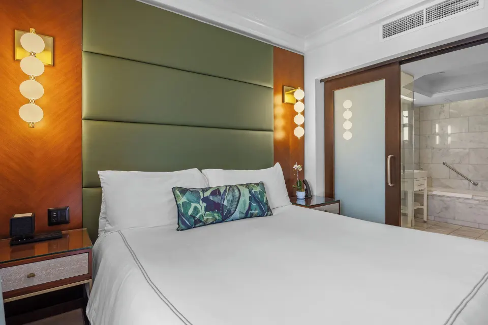 Guest room with bed, green padded headboard and glass bathroom door at Condado Vanderbilt Hotel.