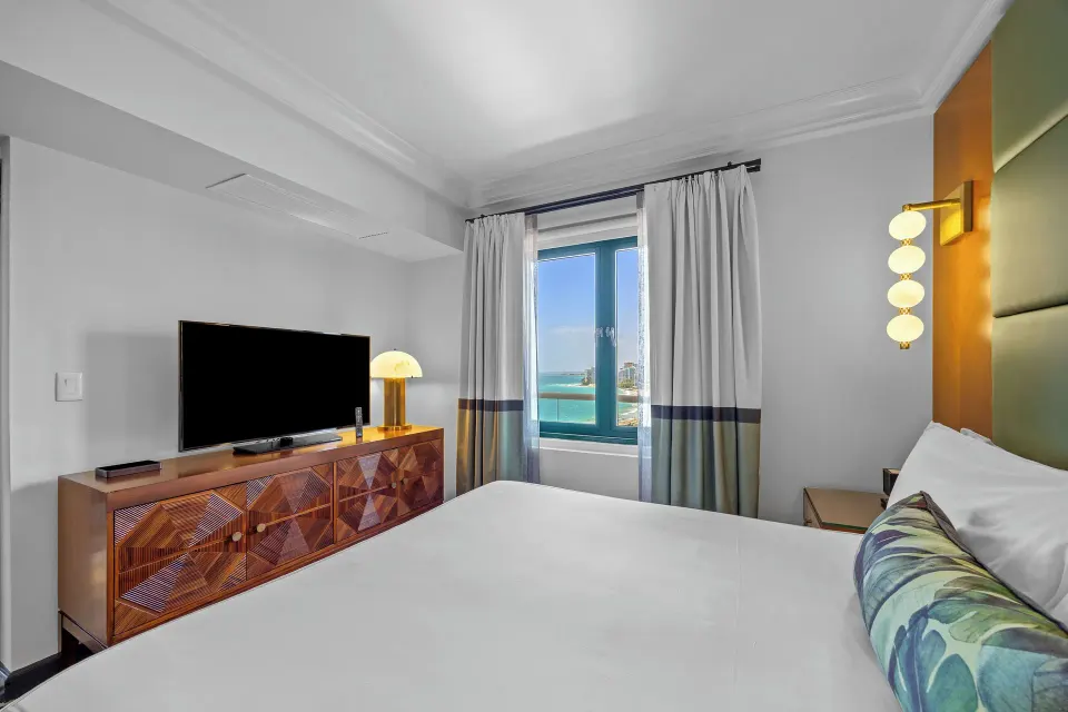 King bed, TV console, and ocean-view window in a guest room at Condado Vanderbilt Hotel.