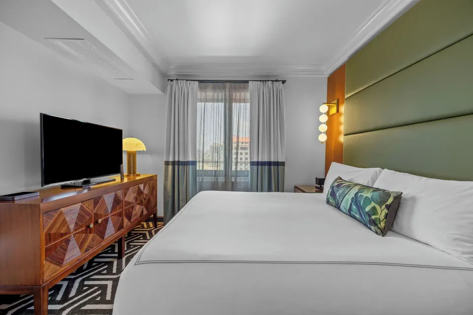 Guest room with king bed, patterned carpet, TV console and window at Condado Vanderbilt Hotel.