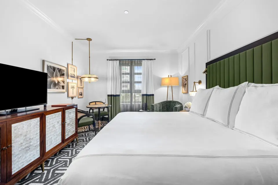 King guest room at Condado Vanderbilt Hotel with sofa, small dining table, TV, and framed wall art.