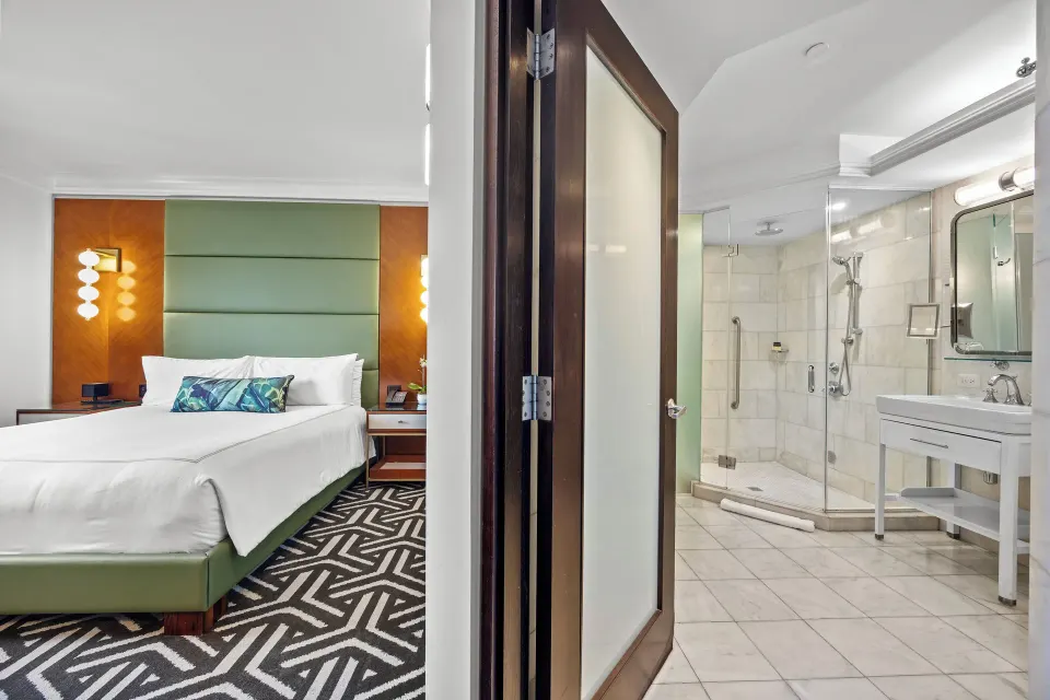 King guest room and white-tiled bathroom at Condado Vanderbilt Hotel seen through an open doorway.