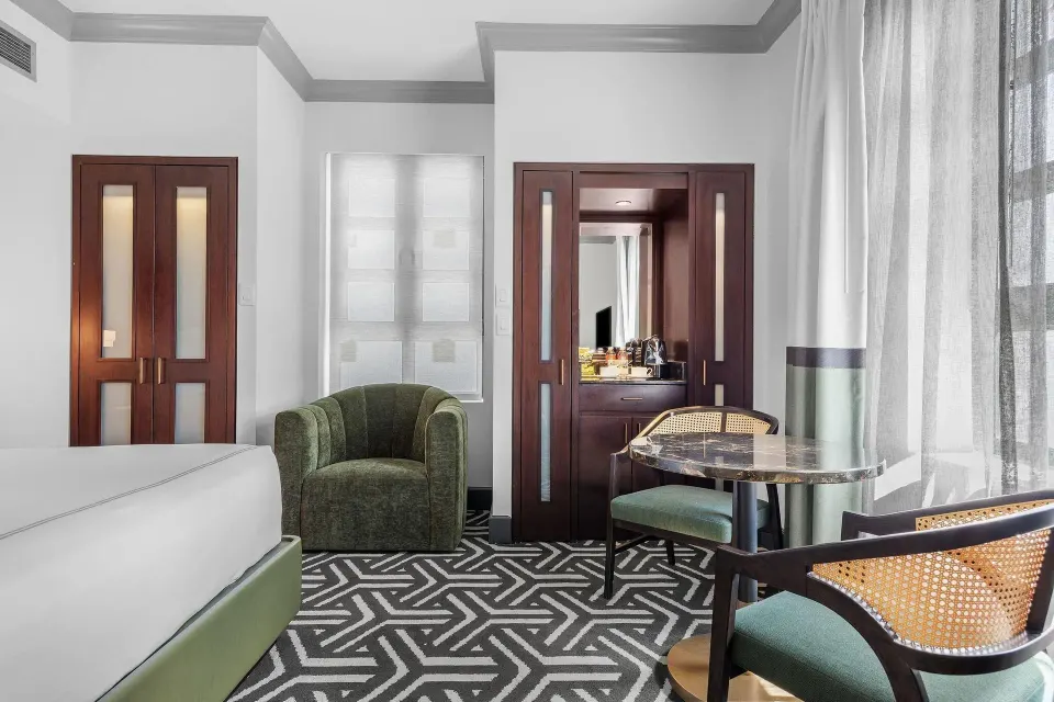 Guest room with a bed, seating area, patterned carpet, and tall windows at Condado Vanderbilt Hotel.