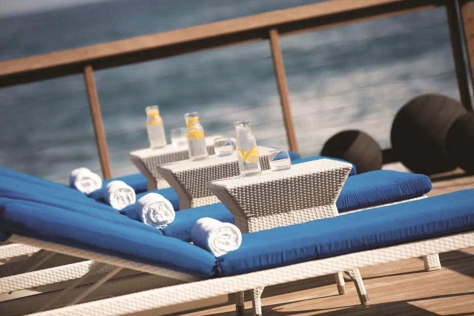 Blue cushioned loungers with drinks beside the ocean at Condado Vanderbilt Hotel.