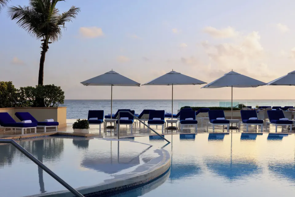 Oceanfront pool with white umbrellas and blue loungers at Condado Vanderbilt Hotel.