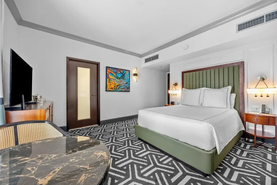 Spacious guest room with bed, dresser, artwork and adjoining doorway at Condado Vanderbilt Hotel.