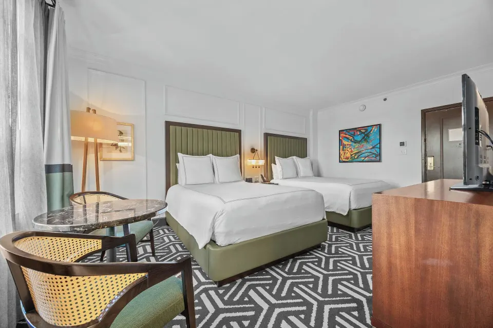 Two-bed guest room with cane chairs, glass table, and TV console at Condado Vanderbilt Hotel.