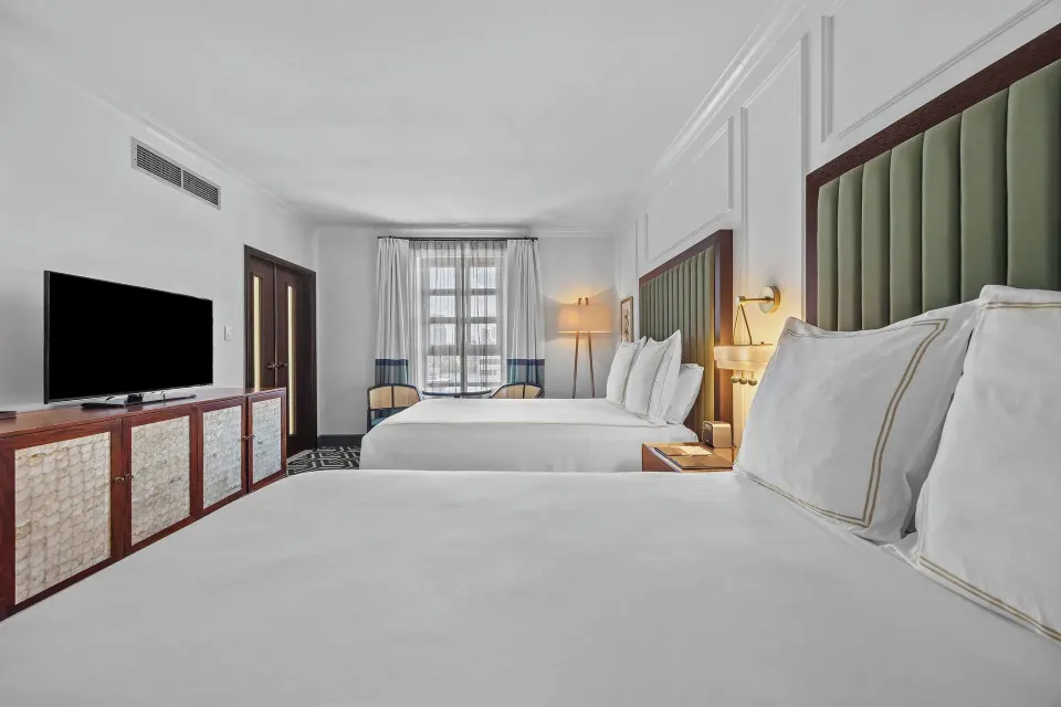 Two-bed guest room with green headboards and long media console at Condado Vanderbilt Hotel.