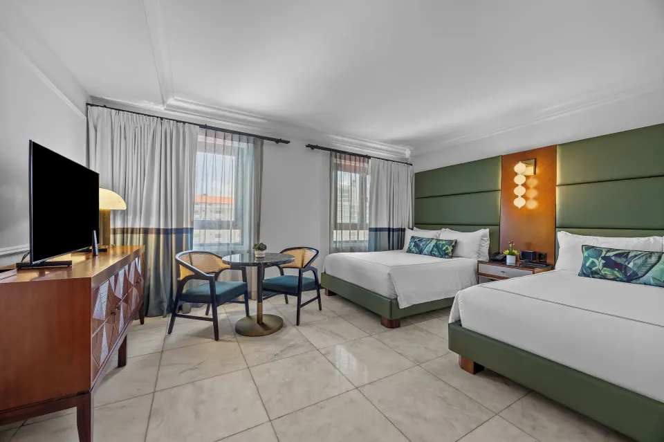 Two-bed guest room with media console and window seating area at Condado Vanderbilt Hotel.