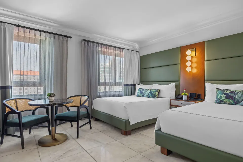 Two-bed guest room with green headboards and round table at Condado Vanderbilt Hotel.