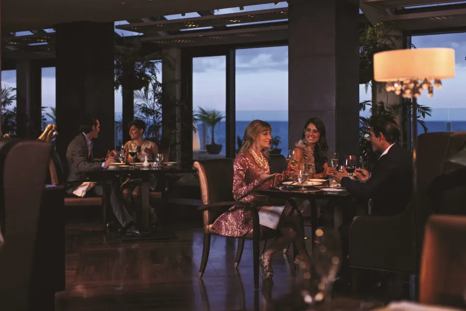 Guests dining by large ocean-facing windows at Condado Vanderbilt Hotel.
