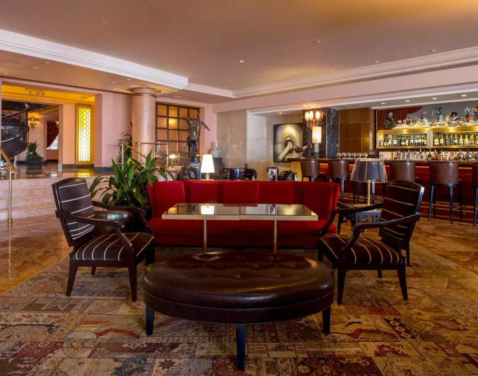 Lobby bar seating with red sofa and patterned rug at Condado Vanderbilt Hotel.