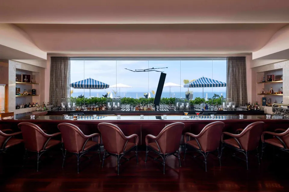Ocean-view bar with red chairs and striped umbrellas at Condado Vanderbilt Hotel.