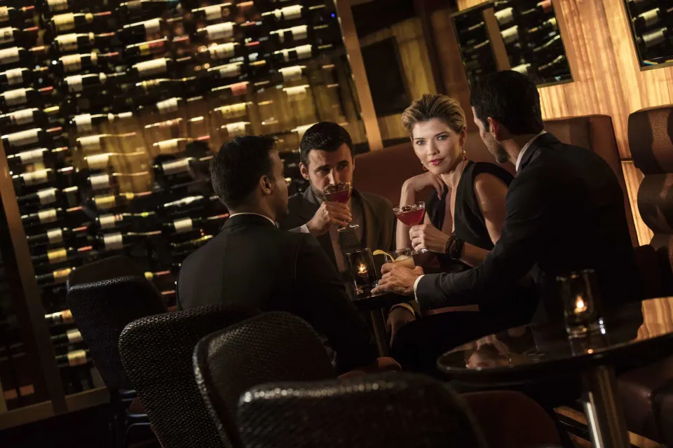 Guests with drinks beside a wall of wine bottles at Condado Vanderbilt Hotel.