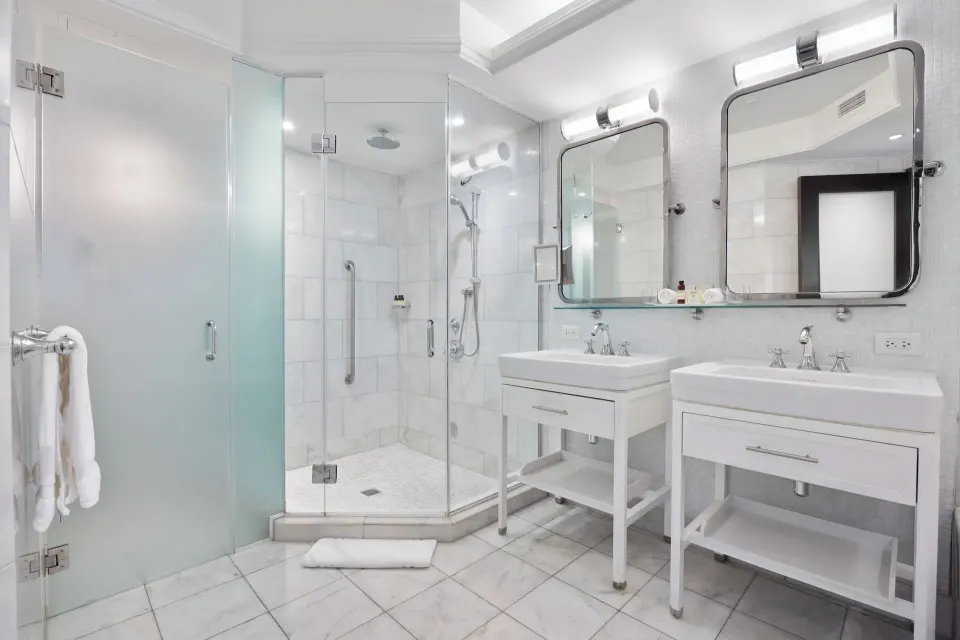 White suite bathroom with twin vanities and corner shower at Condado Vanderbilt Hotel.