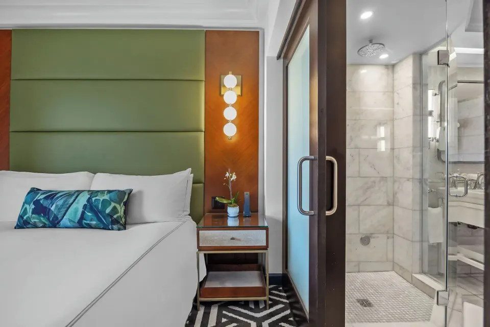 King bed beside a glass shower in the Commodore City View Suite at Condado Vanderbilt Hotel.