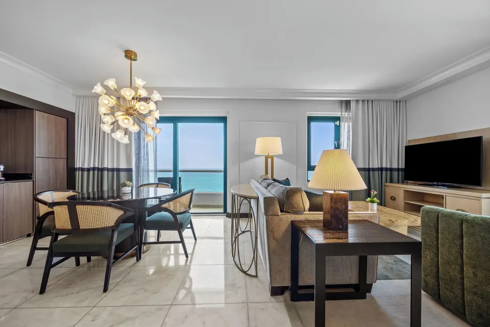 Living room with sofa bed, dining table, TV, and ocean view at Condado Vanderbilt Hotel.