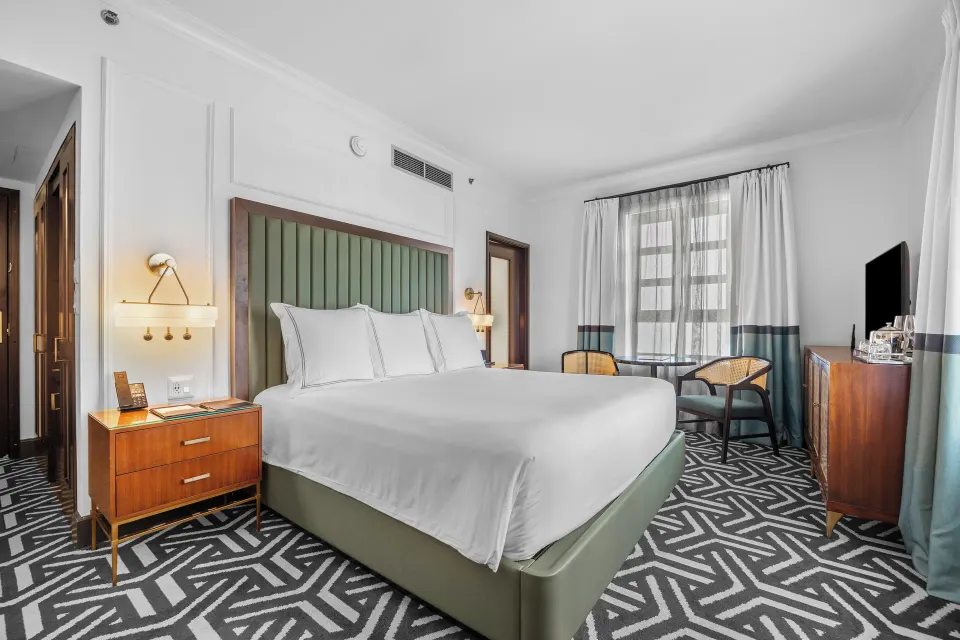 Heritage Queen Room with queen bed, nightstand, seating by the window, and TV at Condado Vanderbilt Hotel.