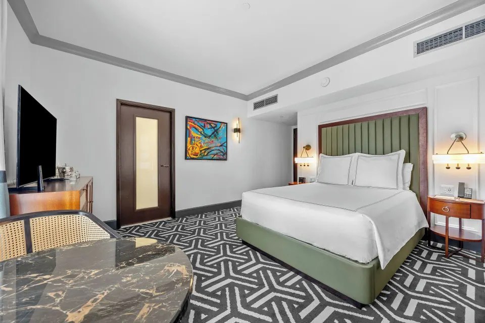 Heritage Queen Room with queen bed, marble-top table, TV, and colorful wall art at Condado Vanderbilt Hotel.